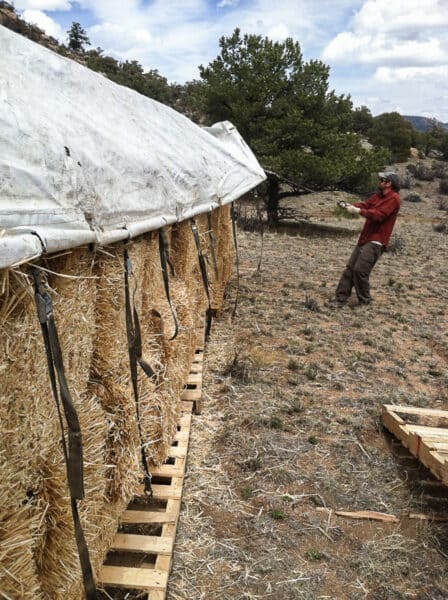 Anchoring the edges of a hay tarp on a strawbale stack for construction in straw houses.
