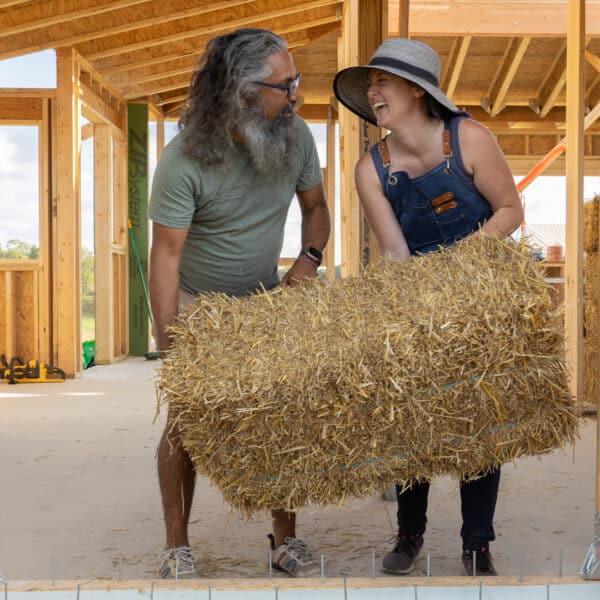 Two people lifting a strawbale together for installation in a straw house.
