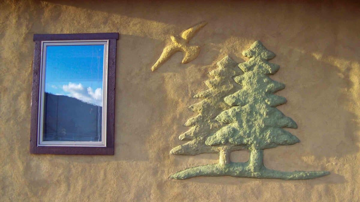Strawbale home wall exterior plaster art of a bird and evergreen trees
