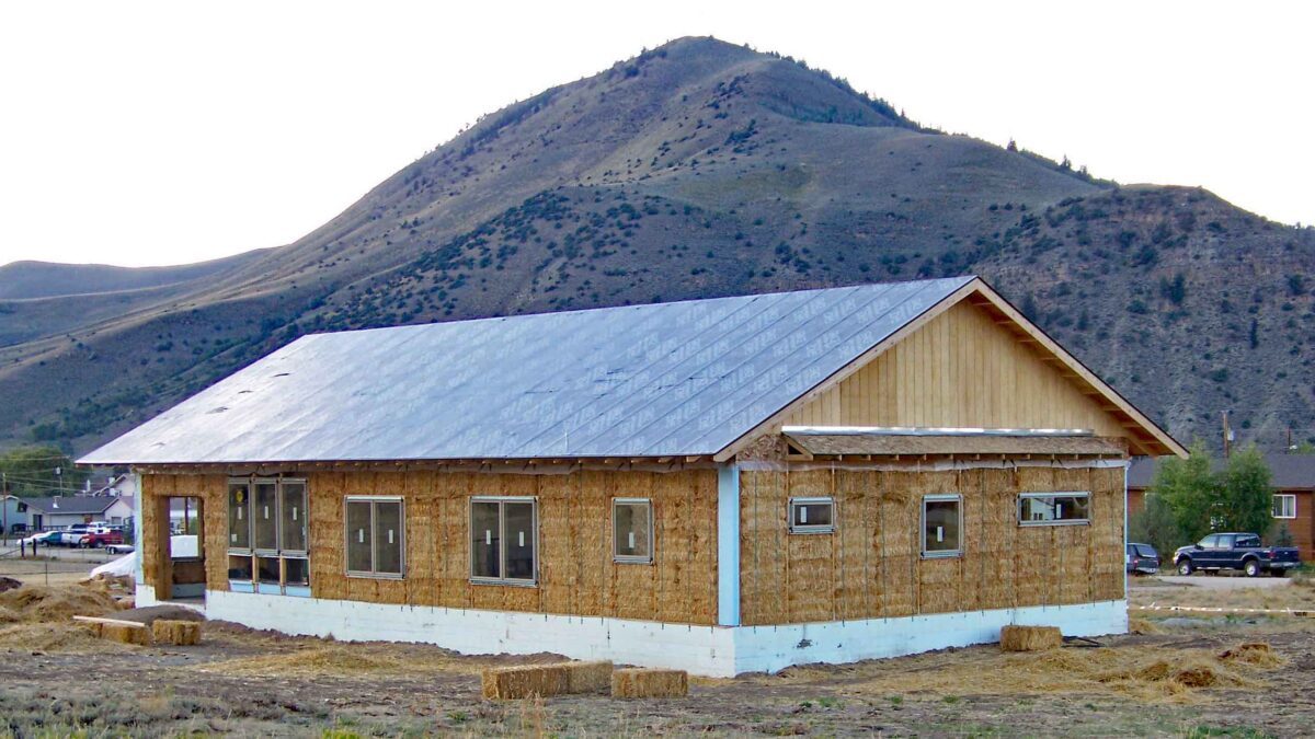 Straw bale house with bales installed, simple roofline with mountain in background.