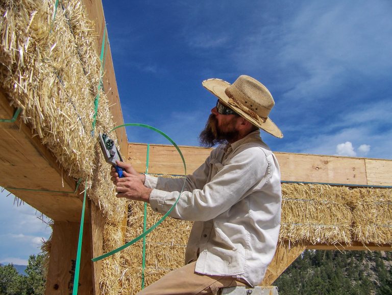 strawbale home construction. tightening bale straps to foundation