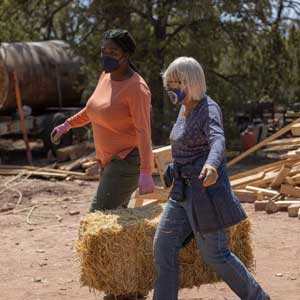 Two women carrying a straw bale at a hands-on workshop